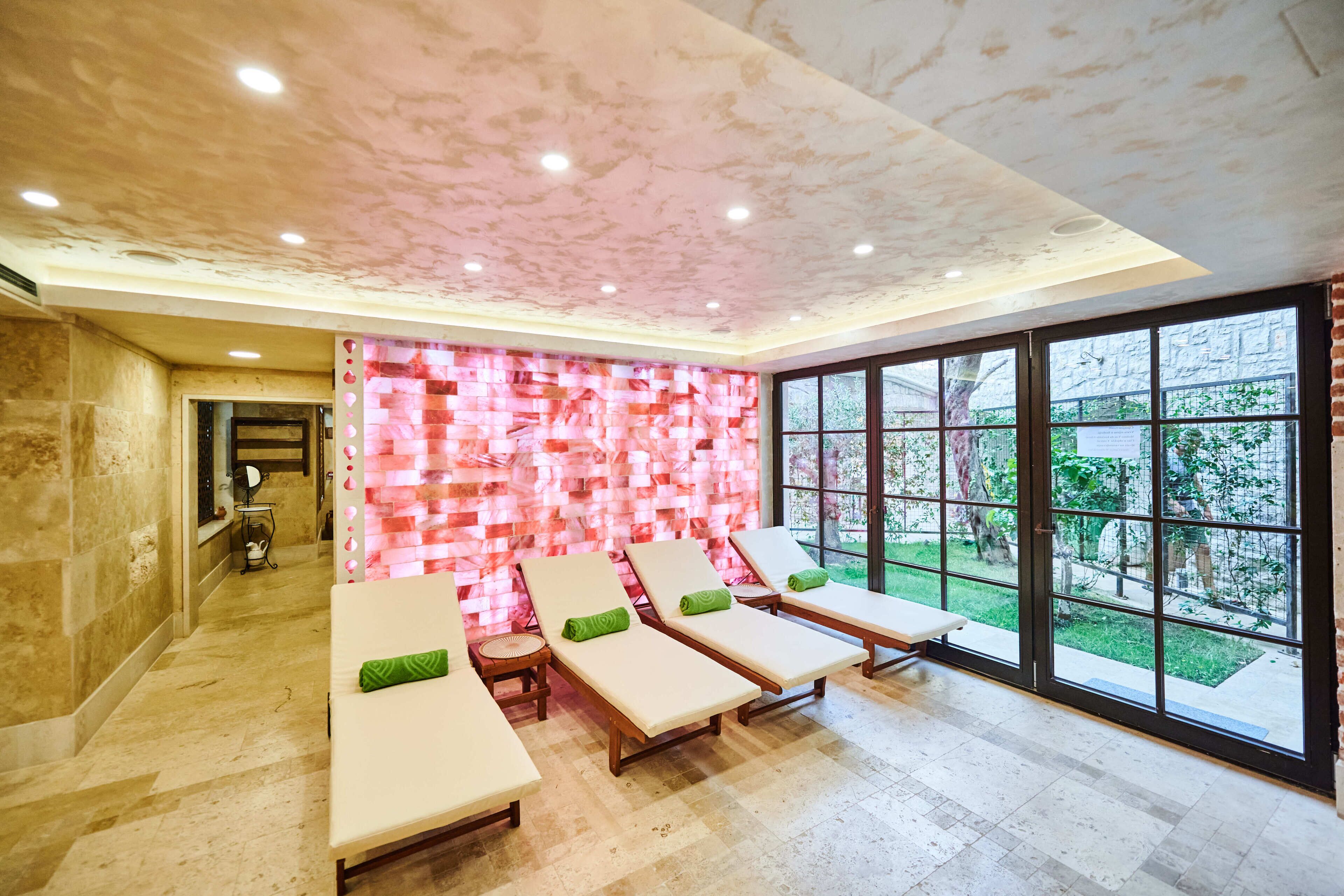 Une salle de spa équipée de quatre chaises longues, d’une table de massage et d’une grande fenêtre donnant sur l’extérieur.
