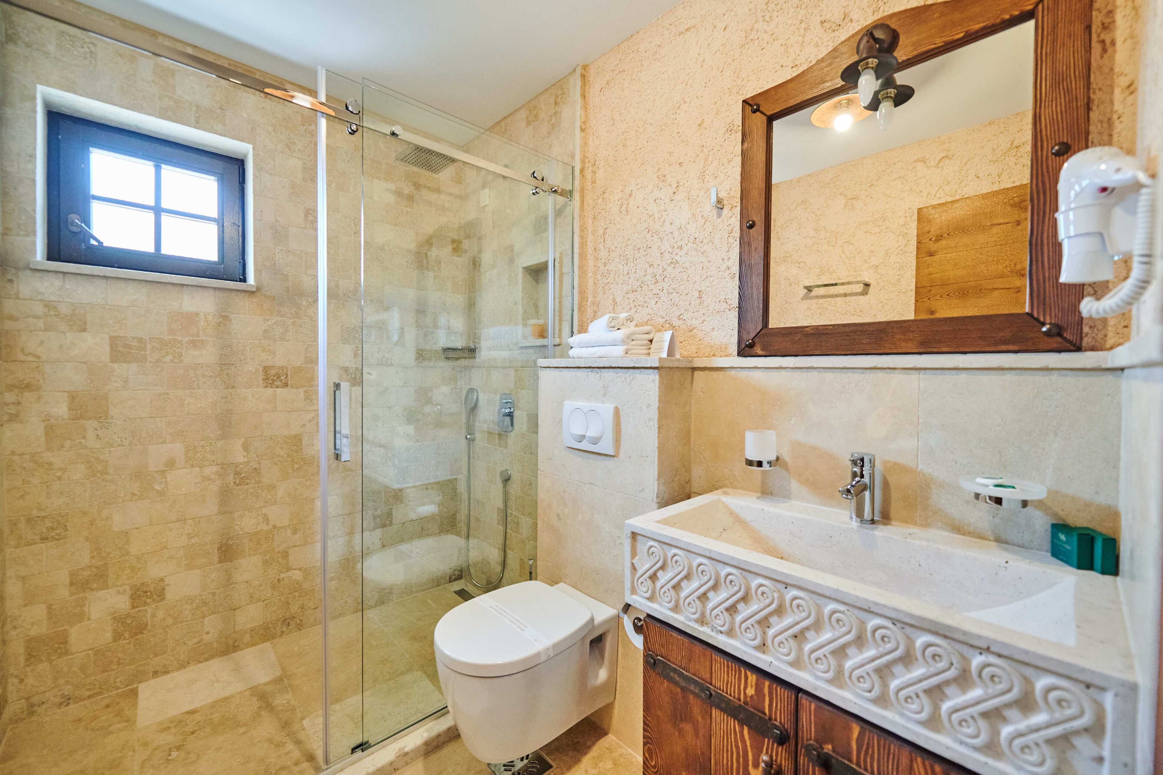 A bathroom with a glass shower enclosure, a white toilet, a sink with a wooden vanity, and a mirror with a wooden frame.