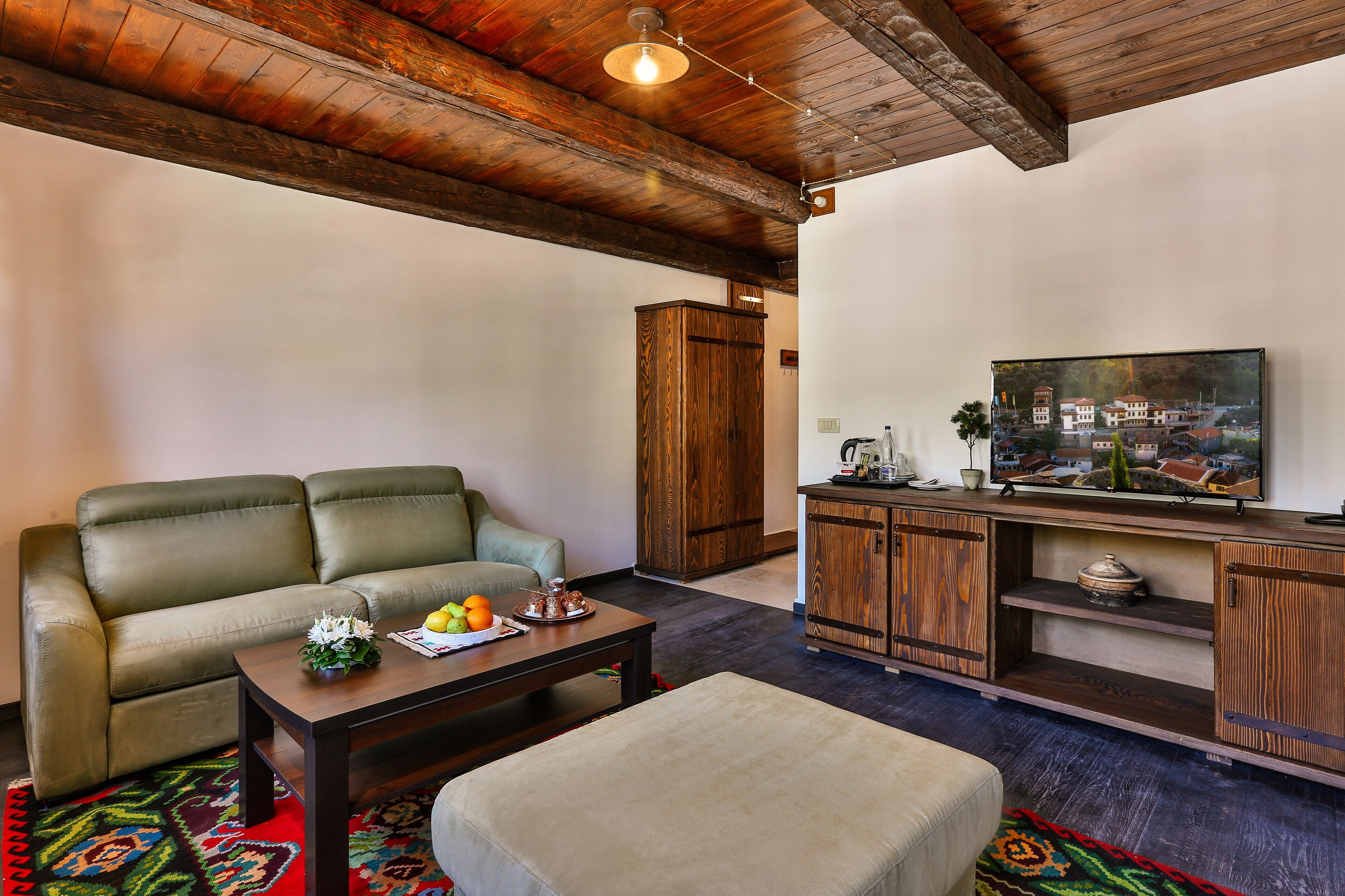 Una sala de estar con un sofá, una mesa de centro, un reposapiés, un aparador de madera y una televisión.