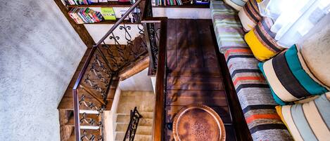 A staircase with a metal railing leading to a lower level, a wooden coffee table with a copper bowl, and a sofa with striped cushions.