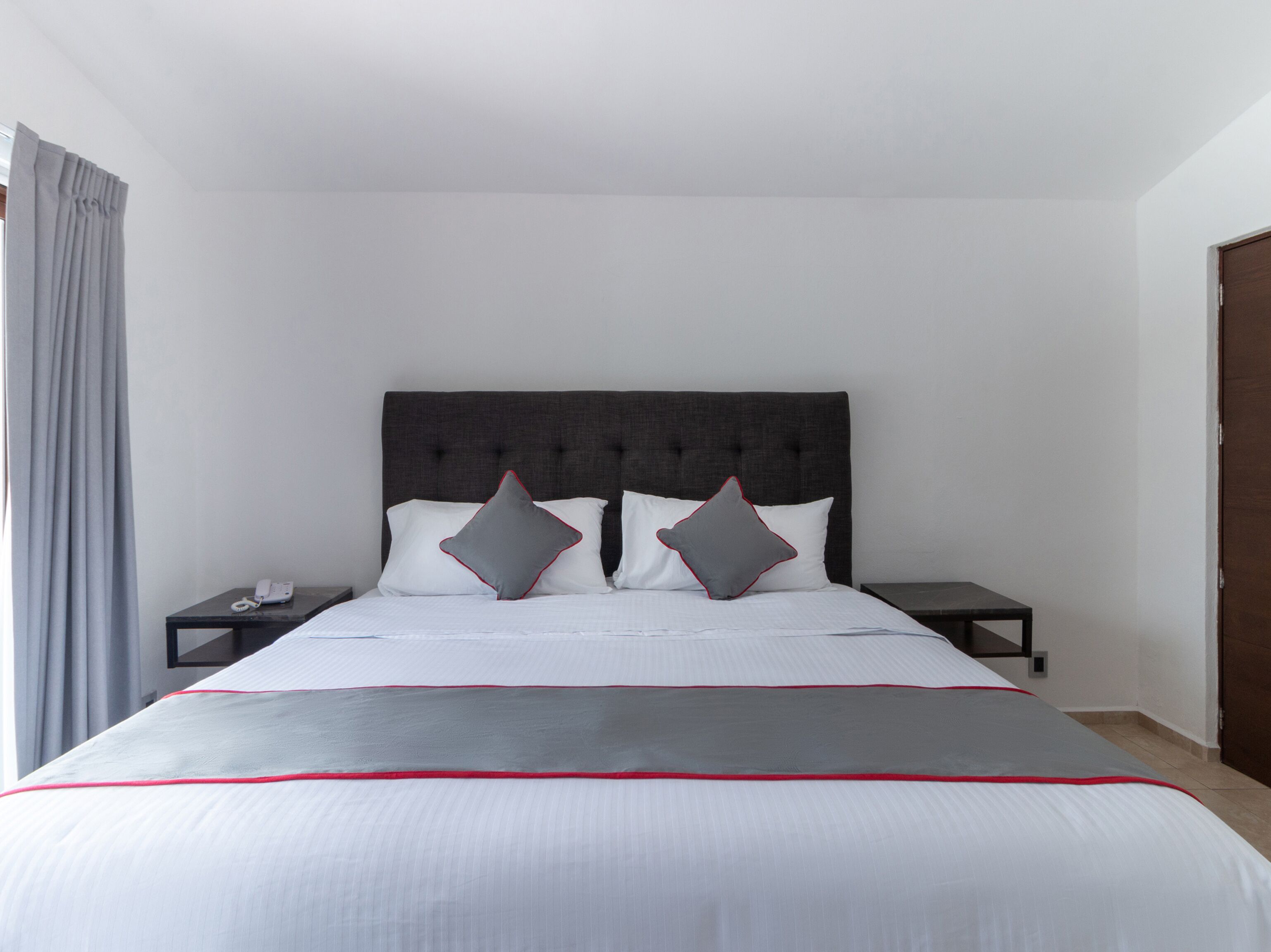 Una habitación de hotel con una cama grande, dos mesitas de noche y un cabecero oscuro.