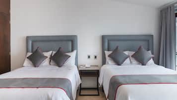 Hotellihuoneessa on kaksi sänkyä, joissa on harmaa pääty, valkoiset vuodevaatteet ja harmaat tyynyt, joissa on punainen reunus. Sänkyjen välissä on yöpöytä, jossa on puhelin, sekä pieni pöytä.