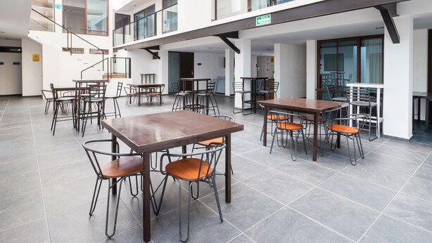 A spacious indoor area with multiple tables and chairs, a staircase, and large windows. - Fraga Hotel Boutique (Irapuato)