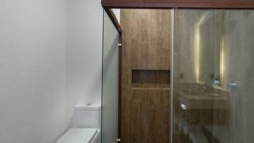 Un baño moderno con cabina de ducha de vidrio, inodoro blanco y tocador de madera.