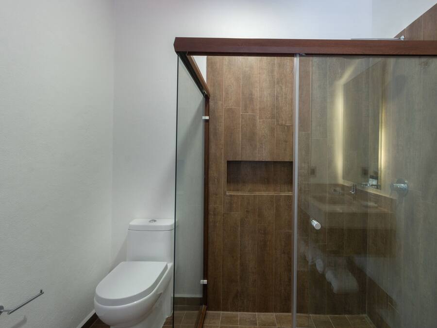 Un baño moderno con cabina de ducha de vidrio, inodoro blanco y tocador de madera.