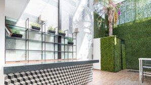A modern reception area with a geometric patterned wall, a glass display shelf with potted plants, and a neatly tiled floor. - Fraga Hotel Boutique (Irapuato)