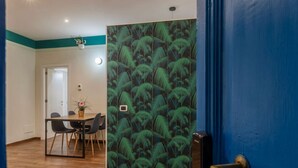 Una habitación con una mesa de comedor, sillas, una puerta azul y una pared con un diseño de hojas verdes.