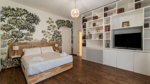 Un dormitorio con cama, televisor, estantería y una pared con un mural floral.