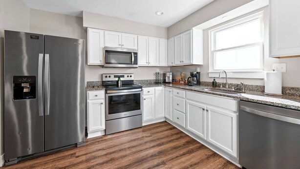 A modern kitchen with stainless steel appliances, white cabinetry, and a granite countertop.
