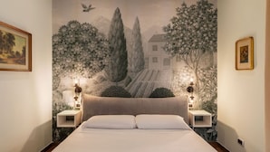 Een slaapkamer met een groot bed, twee nachtkastjes met lampen, een muurschildering en ingelijste foto's aan de wand.