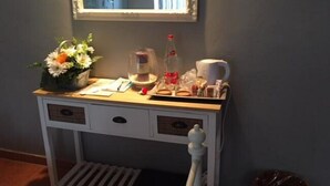 Een klein, wit houten bureau met daarboven een spiegel, een bloevas, een fles en wat papieren.