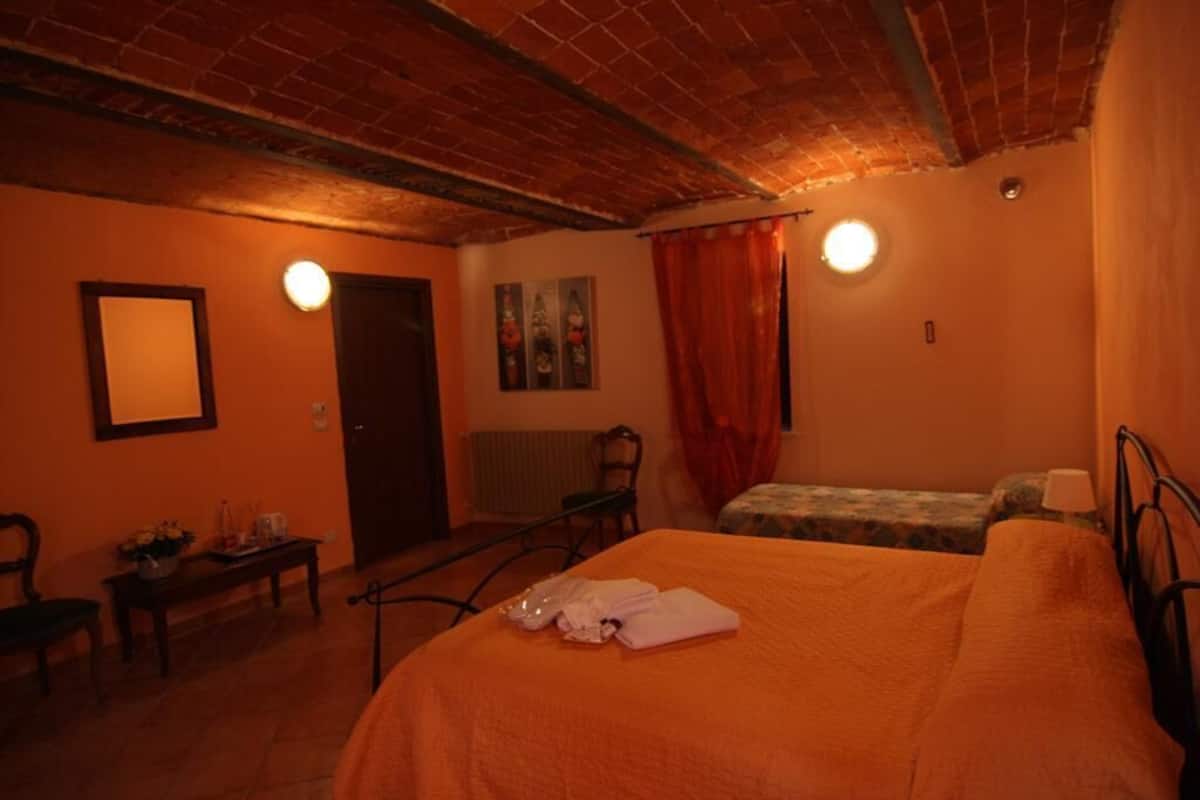 Una habitación con techo de ladrillo, una cama con colcha naranja, una mesita con una silla y un radiador.