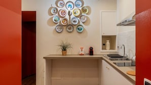 Une cuisine compacte avec une collection d’assiettes décoratives accrochées au mur, une petite plante et une machine à café.