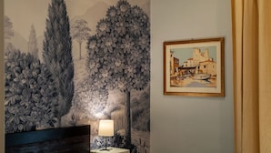 Une pièce décorée d’une fresque représentant un paysage, d’un tableau encadré représentant une scène côtière et d’une lampe posée sur une table.