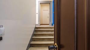 Un escalier menant à une pièce dotée d’une porte, une télécommande posée sur le sol et un appareil fixé au mur.
