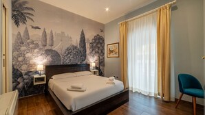 Une chambre avec un grand lit, deux tables de chevet, une commode, une chaise, une fresque murale et une fenêtre avec des rideaux.
