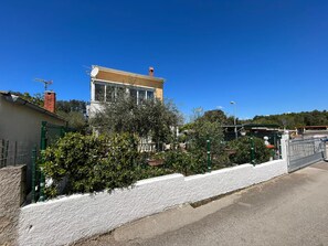 A two-story building with a yellow facade and a brick chimney, surrounded by greenery and a white fence. - Apartments Kekic (Zadar)
