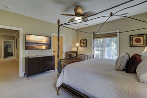Une chambre à coucher avec un lit à baldaquin, un téléviseur fixé au mur et une grande fenêtre donnant sur un paysage verdoyant.
