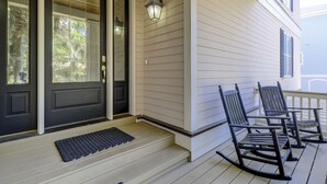 Une véranda avec deux fauteuils à bascule et une porte noire dotée de panneaux de verre.