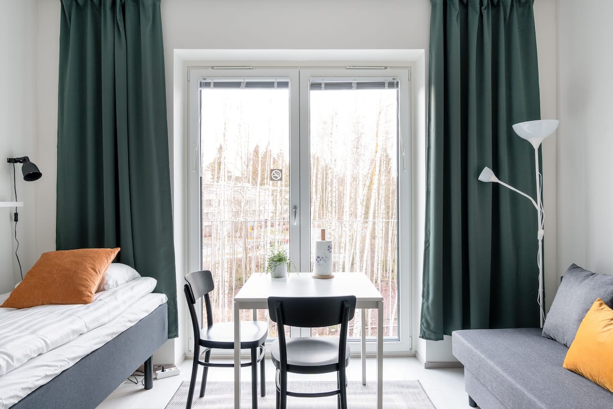 Ein Zimmer mit einem Bett, einem Tisch mit Stühlen, einer Couch und einem großen Fenster mit Vorhängen.
