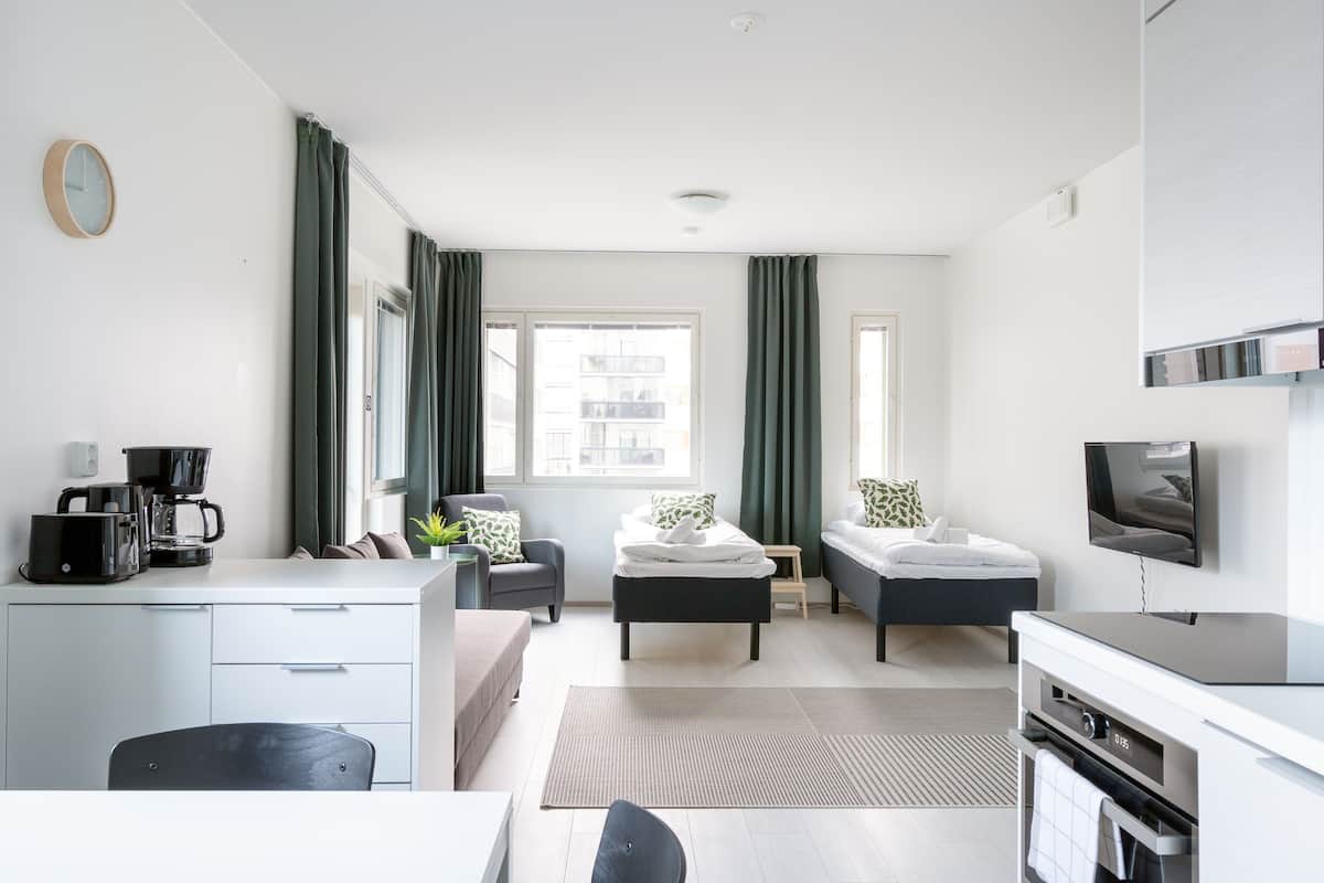 Ein modernes, gut beleuchtetes Zimmer mit einer Küchenzeile, einem Essbereich, einem Bett und einem Fernseher.