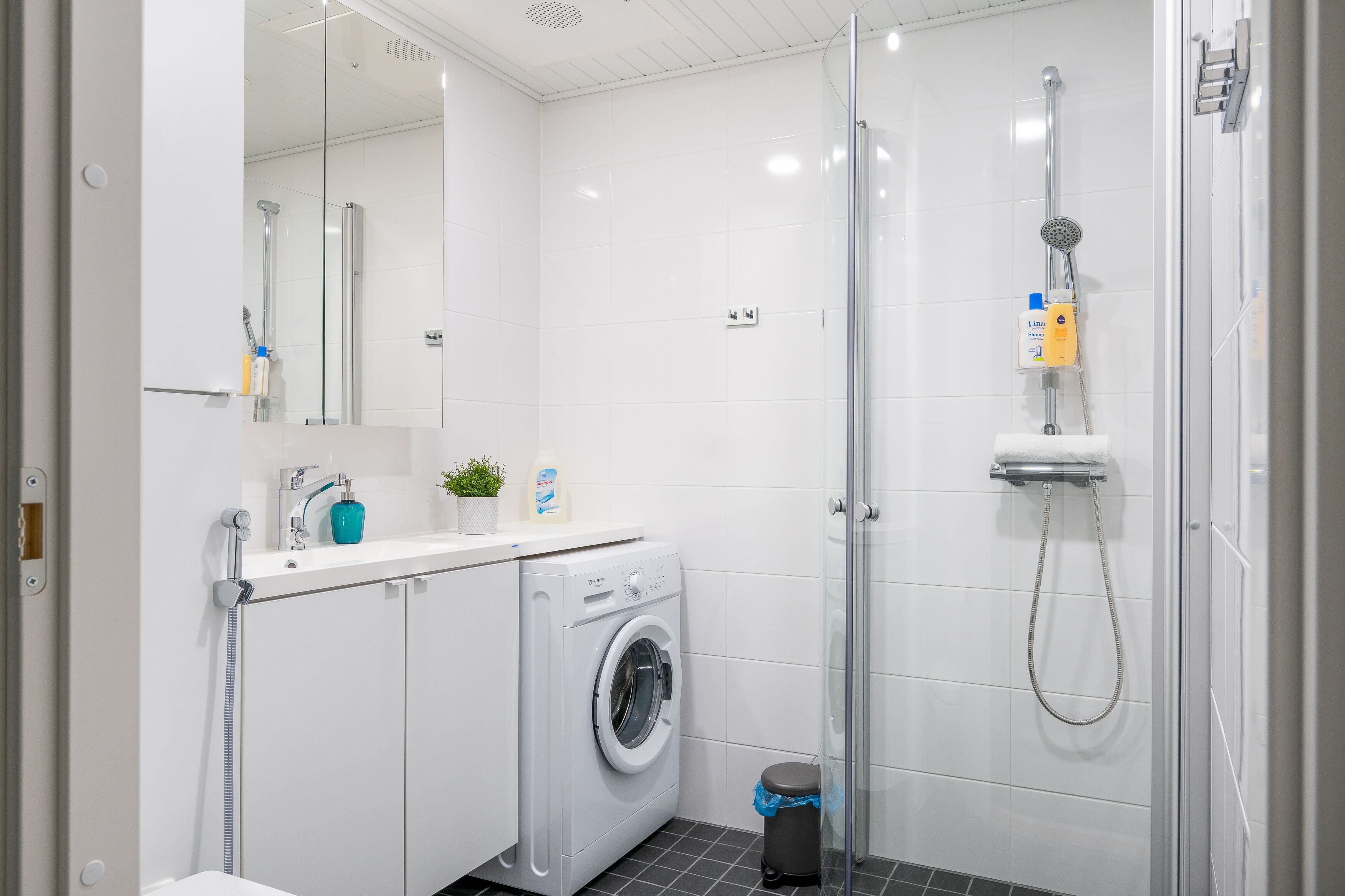 A modern bathroom with a washing machine, a glass shower enclosure, and a sink with a mirror.