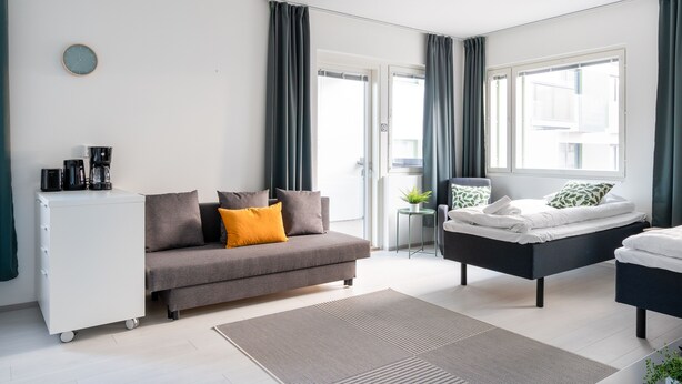 Une chambre à coucher moderne avec un canapé gris, un lit noir, une commode blanche et une petite table d’appoint.