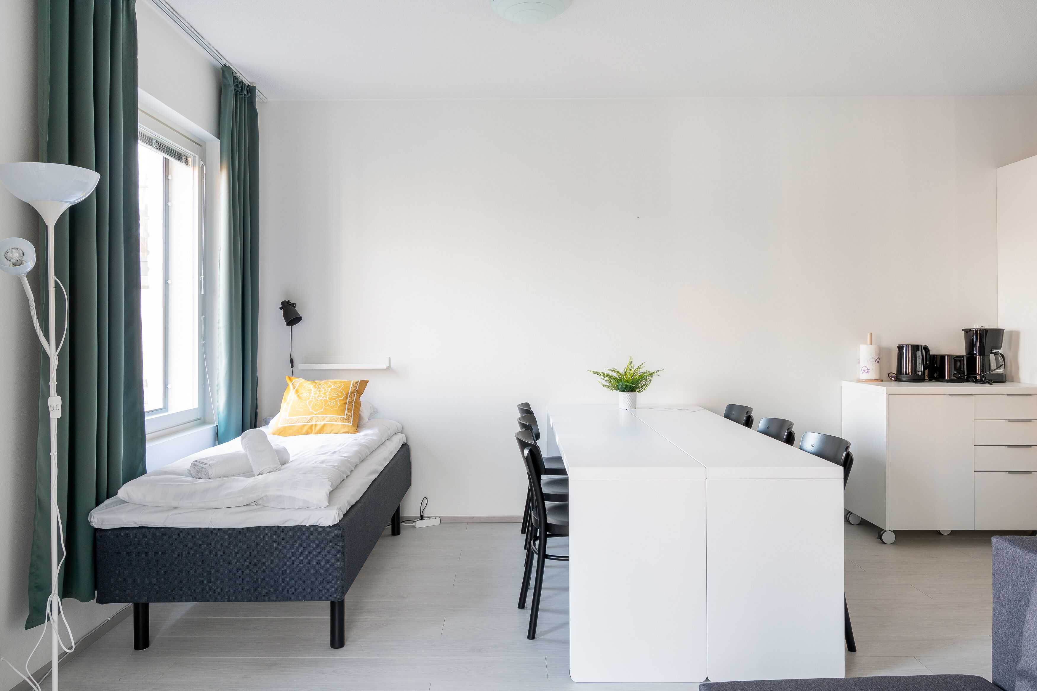 A modern, compact room with a bed, a dining area, and a kitchenette.