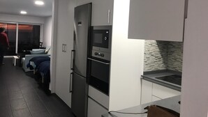 Une cuisine moderne dotée d’appareils électroménagers intégrés, un coin repas avec une table et des chaises, et une personne debout près de la fenêtre.