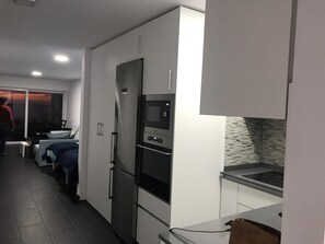 Una cocina moderna con electrodomésticos integrados, una zona de comedor con mesa y sillas, y una persona de pie junto a la ventana.