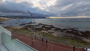 A coastal view with a paved walkway, a metal railing, and a distant shoreline. - Canteras Reef - First sea line (Las Palmas de Gran Canaria)