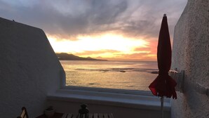 A balcony with a view of the sea at sunset, a table, chairs, and a red umbrella. - Canteras Reef - First sea line (Las Palmas de Gran Canaria)