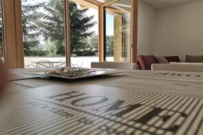 Une pièce avec de grandes fenêtres, une table avec des journaux et un canapé.