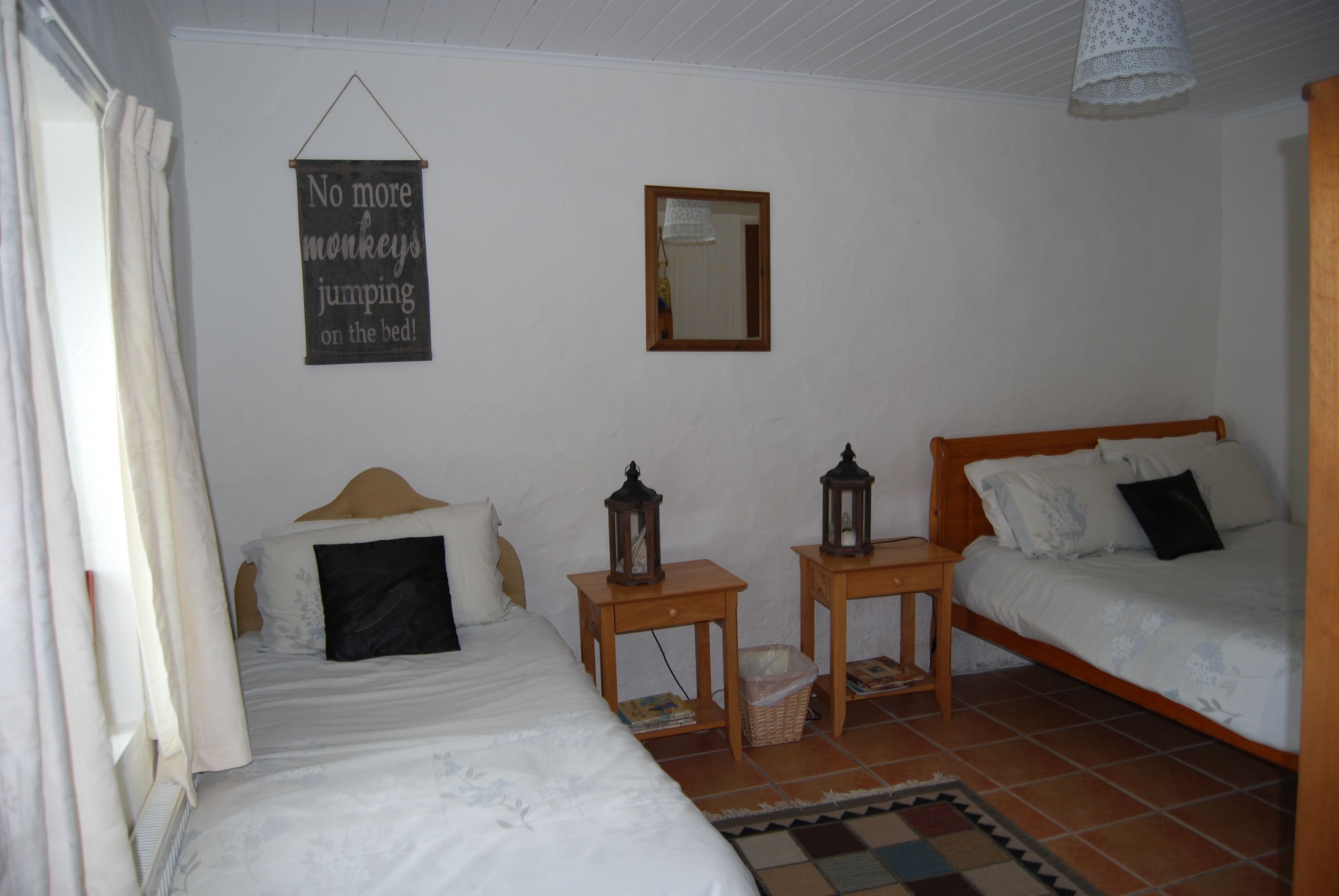 Un dormitorio con dos camas, una mesita con un farol, un espejo y un cartel en la pared.
