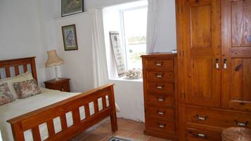 Une chambre à coucher avec un lit en bois, une table de chevet, une commode et une fenêtre avec des rideaux.