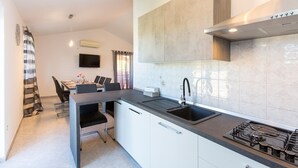 A compact kitchen with a gas stove, a sink, and a dining area with a table and chairs. - A comfortable home perfect for relaxing in the green heart of Istria (Bokordici)