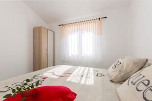 A bedroom with a bed, a wardrobe, and a window with sheer curtains.