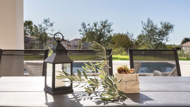 A table with a lantern, a small plant, and a decorative item on a balcony overlooking a pool and houses. - A comfortable home perfect for relaxing in the green heart of Istria (Bokordici)