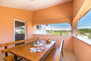 A balcony with a wooden table, benches, and a view of greenery and houses.