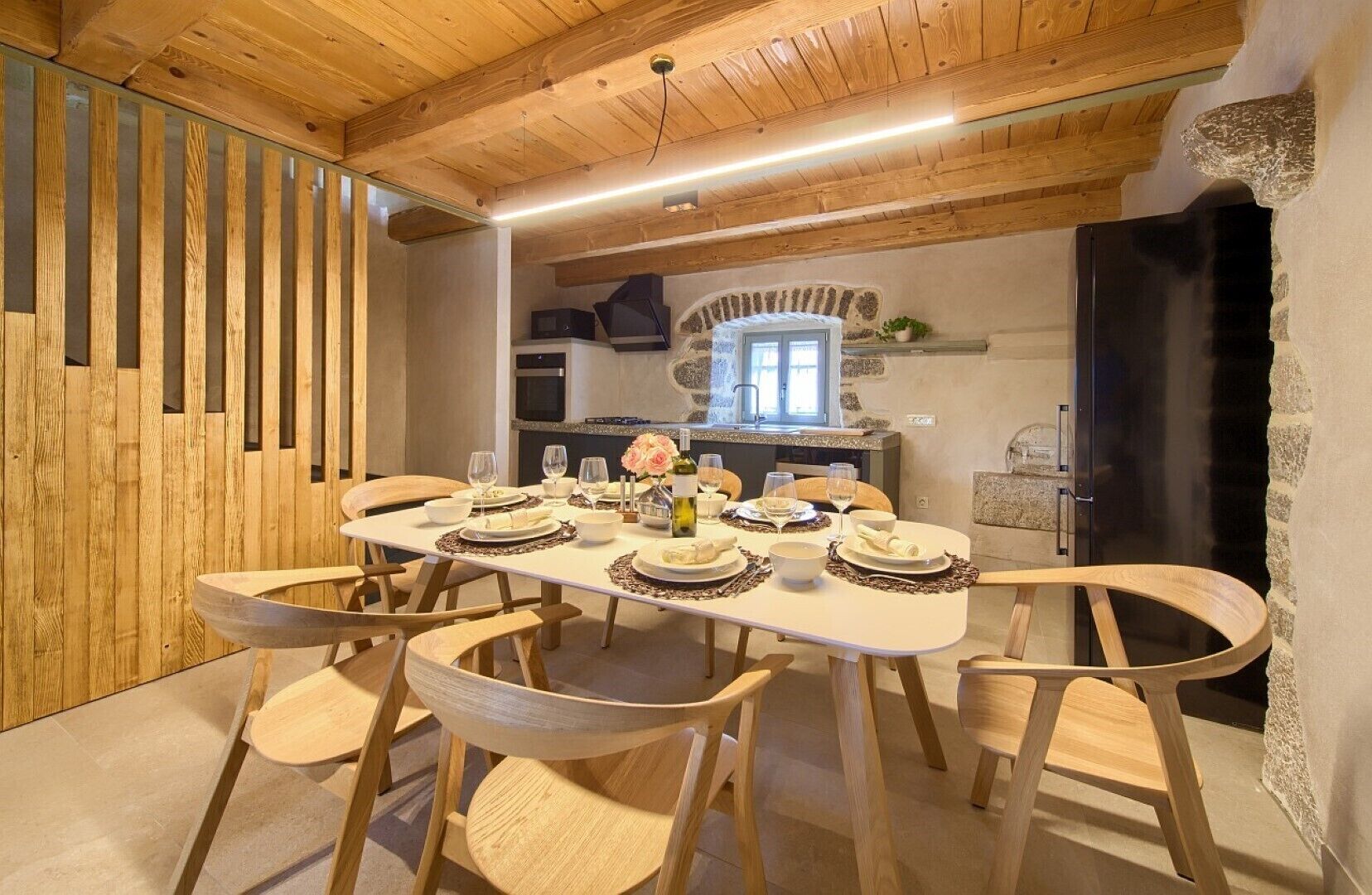 Uma sala de jantar com uma mesa de madeira posta para seis pessoas, rodeada por cadeiras de madeira.