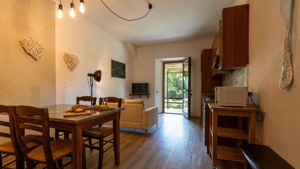 Une cuisine chaleureuse avec des meubles de rangement en bois, une table à manger avec des chaises et un téléviseur fixé au mur.