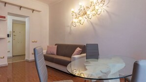 A modern living room with a glass coffee table, a grey sofa with cushions, a wall-mounted light fixture, and a door in the background. - GuestHost - Testaccio Art & Design Flat BOOK NOW! (Roma)