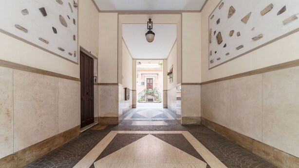 A hallway with a geometric patterned floor, a central light fixture, and stone wall decorations. - GuestHost - Testaccio Art & Design Flat BOOK NOW! (Roma)