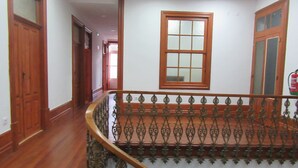 Una escalera de madera con barandillas ornamentales y pasamanos, que conduce a un rellano con un ventanal grande y una puerta.