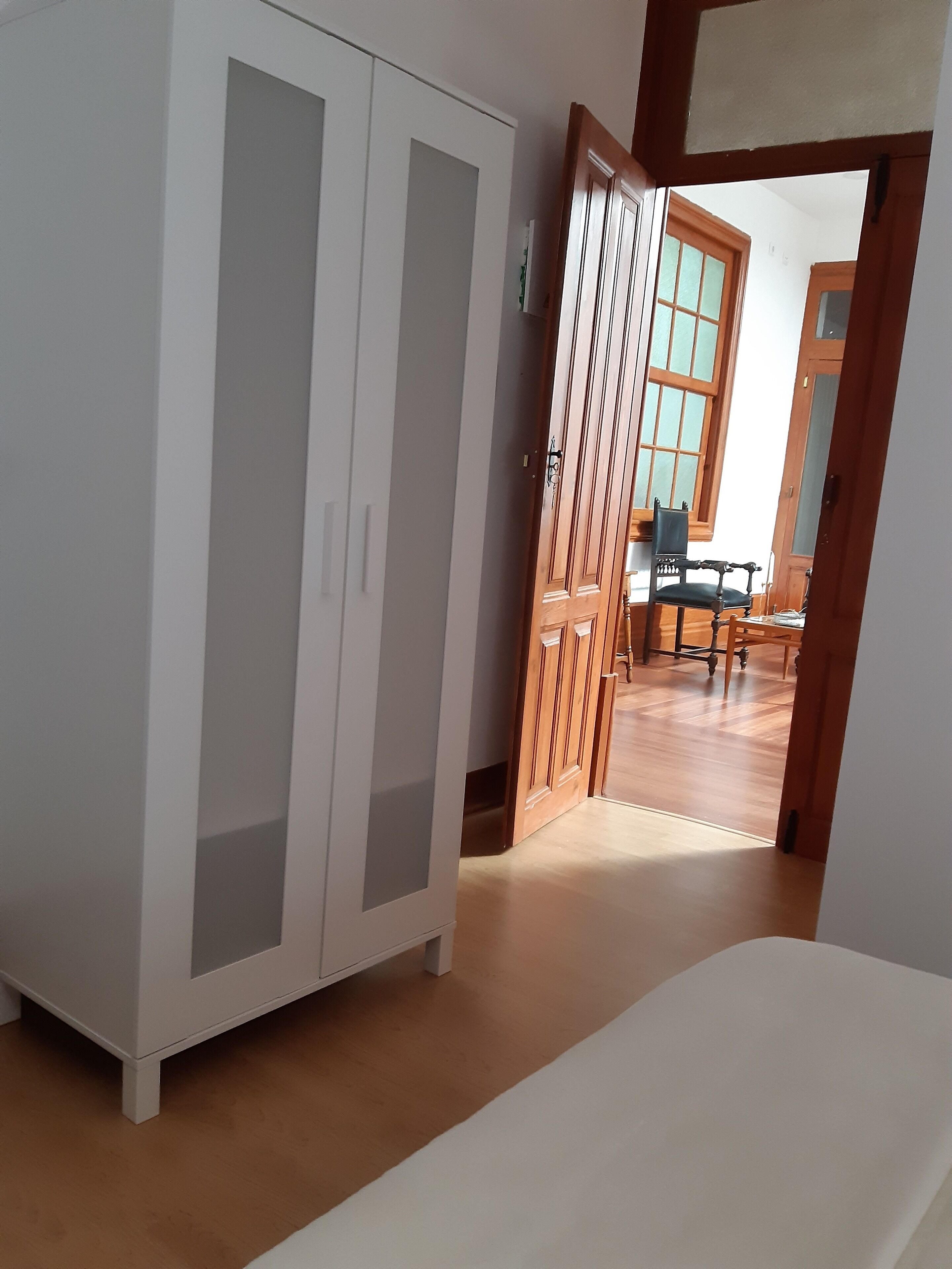Habitación con un armario blanco, una puerta de madera y vistas a un comedor con mesa y sillas.