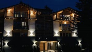 A multi-story building with illuminated balconies and a central entrance. - Apartment "Casa Ester" 4 people (Baselga di Pinè, Italia)