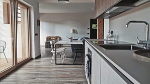 A modern kitchen with a large island, a dining area with a table and chairs, and a view through a sliding door. - Apartment "Casa Ester" 4 people (Baselga di Pinè, Italia)