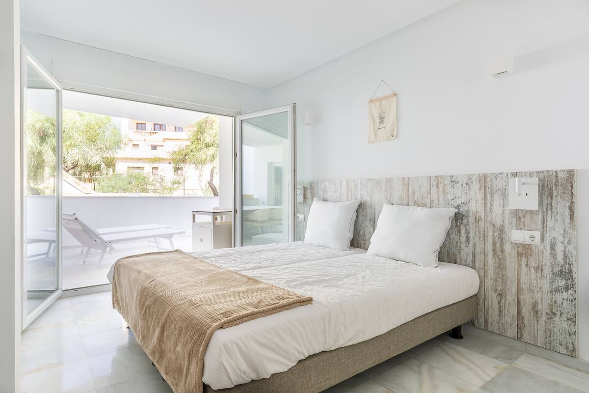 Een moderne slaapkamer met een groot bed, een schuifdeur van glas naar een buitengebied en een rustieke wandpaneel.