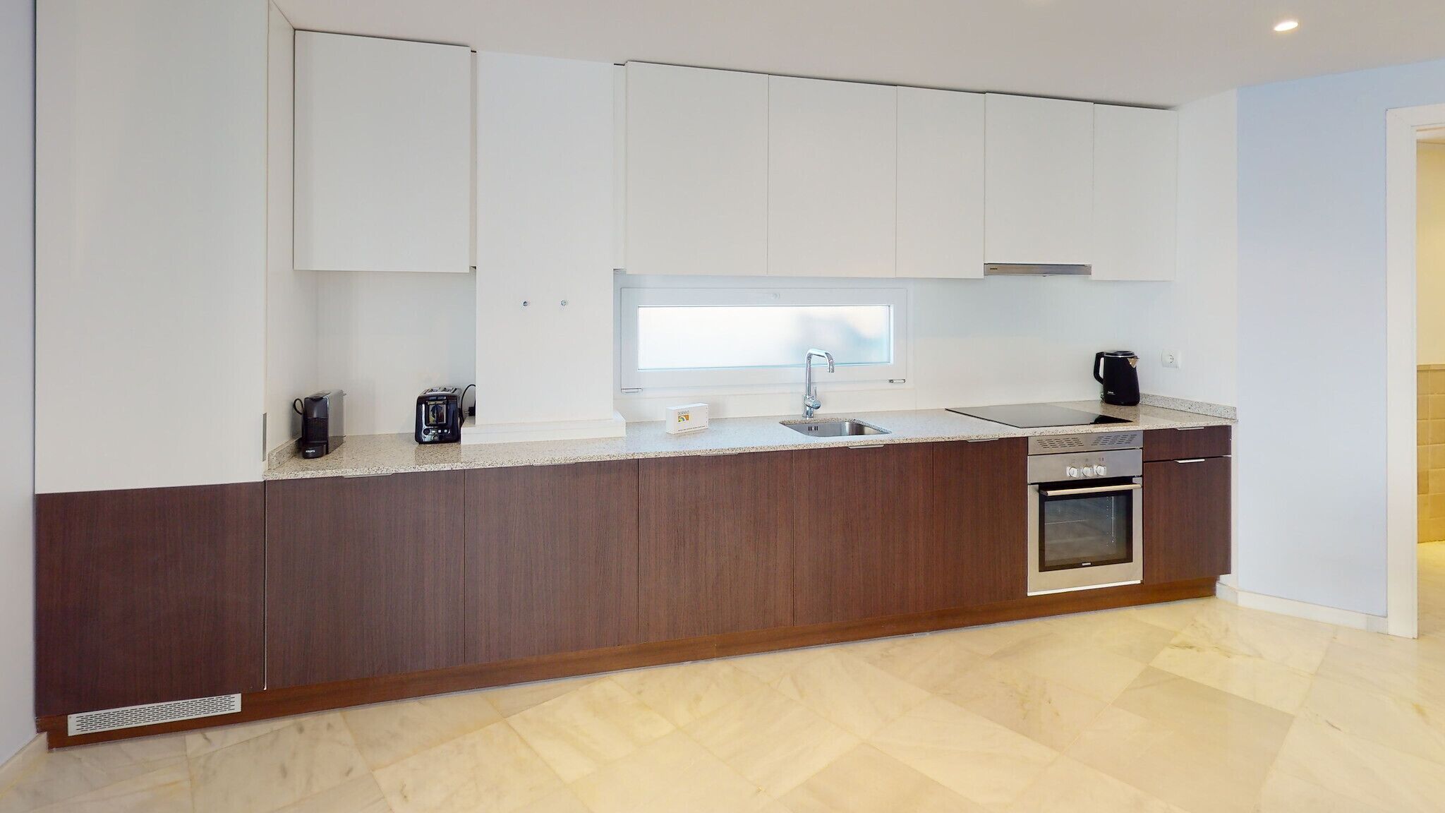 A modern kitchen with a dark wood island, white cabinets, a stainless steel sink, and a built-in oven.