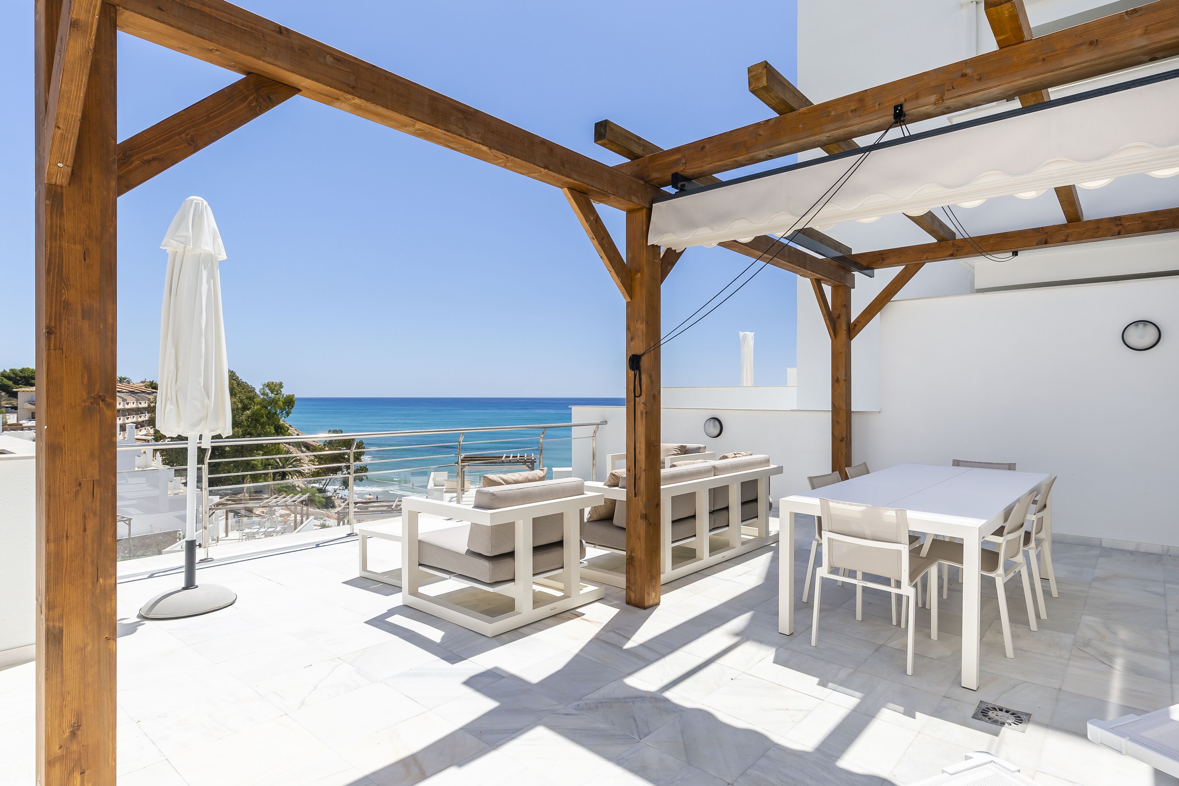 A terrace with white furniture, a white umbrella, and a view of the sea.